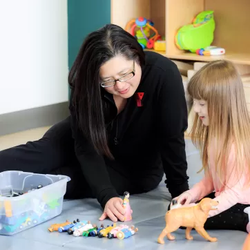 YMCA Child Care Educator and female child playing with animal figures on floor mat